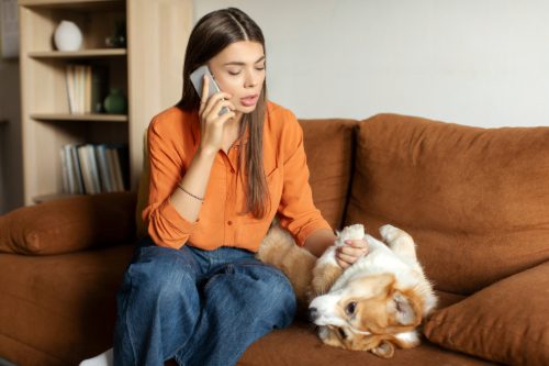 worried female dog owner talking on the phone with the vet while at home petting her dog